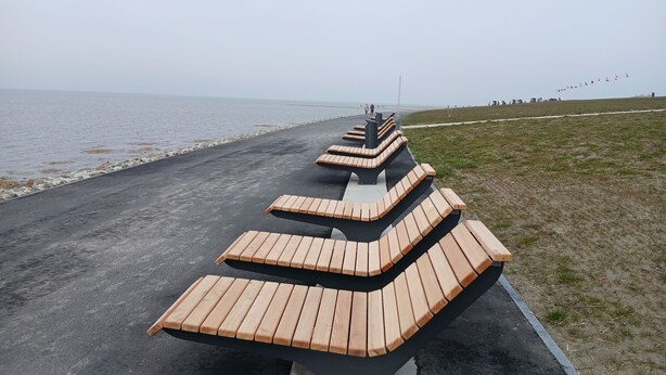 A series of wooden benches arranged in a curved formation along a paved path by the water.
