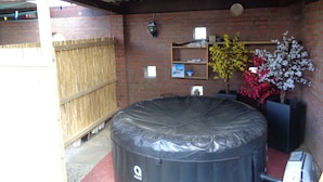 A covered outdoor area with a black inflatable structure, a brick wall, a wooden shelf with items, and a potted plant.