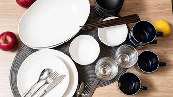 Una mesa de comedor ordenada con platos, cubiertos, palillos, vasos y manzanas.