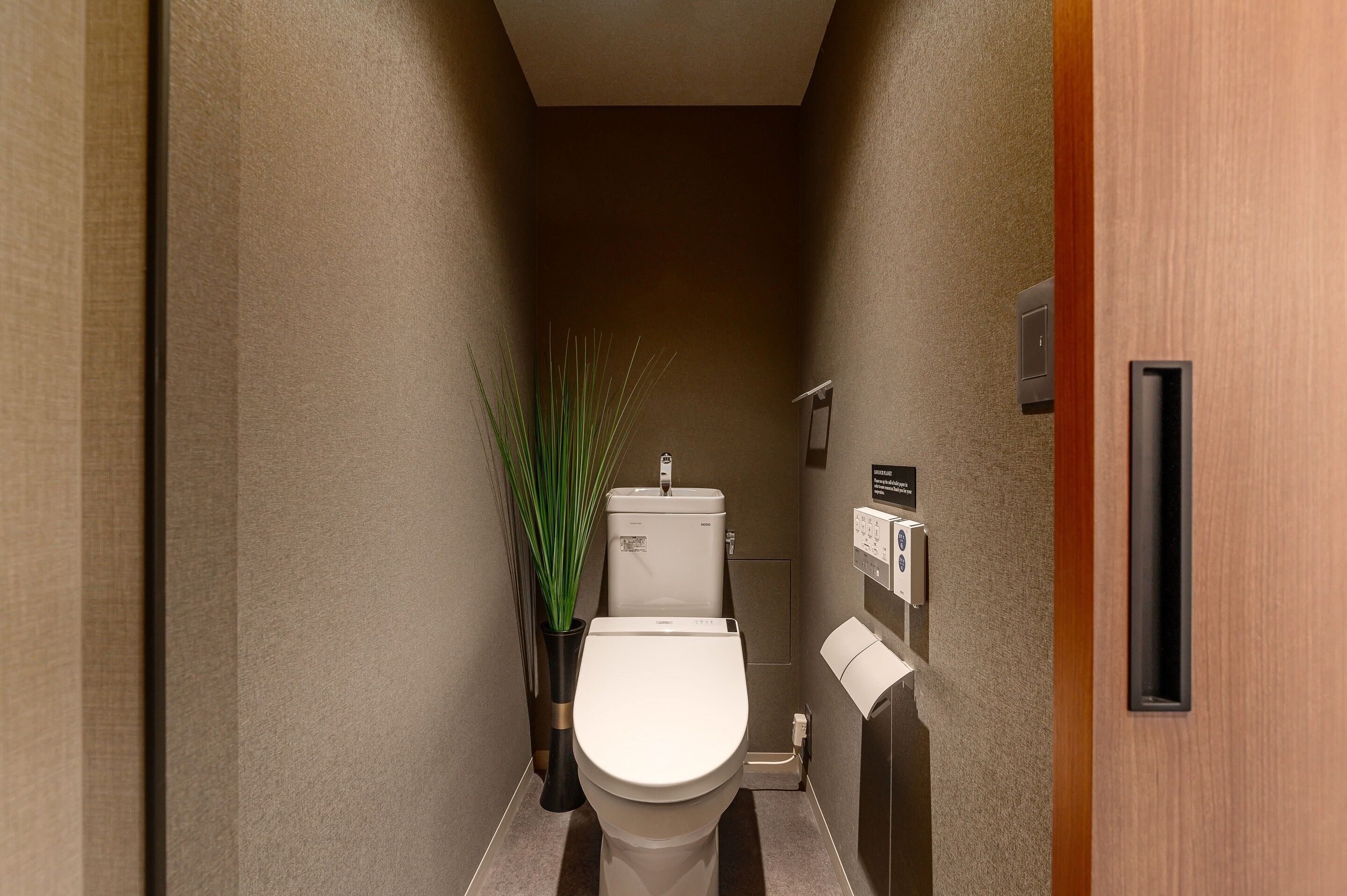 Une salle de bain moderne avec des toilettes, une plante et un distributeur de papier toilette fixé au mur.