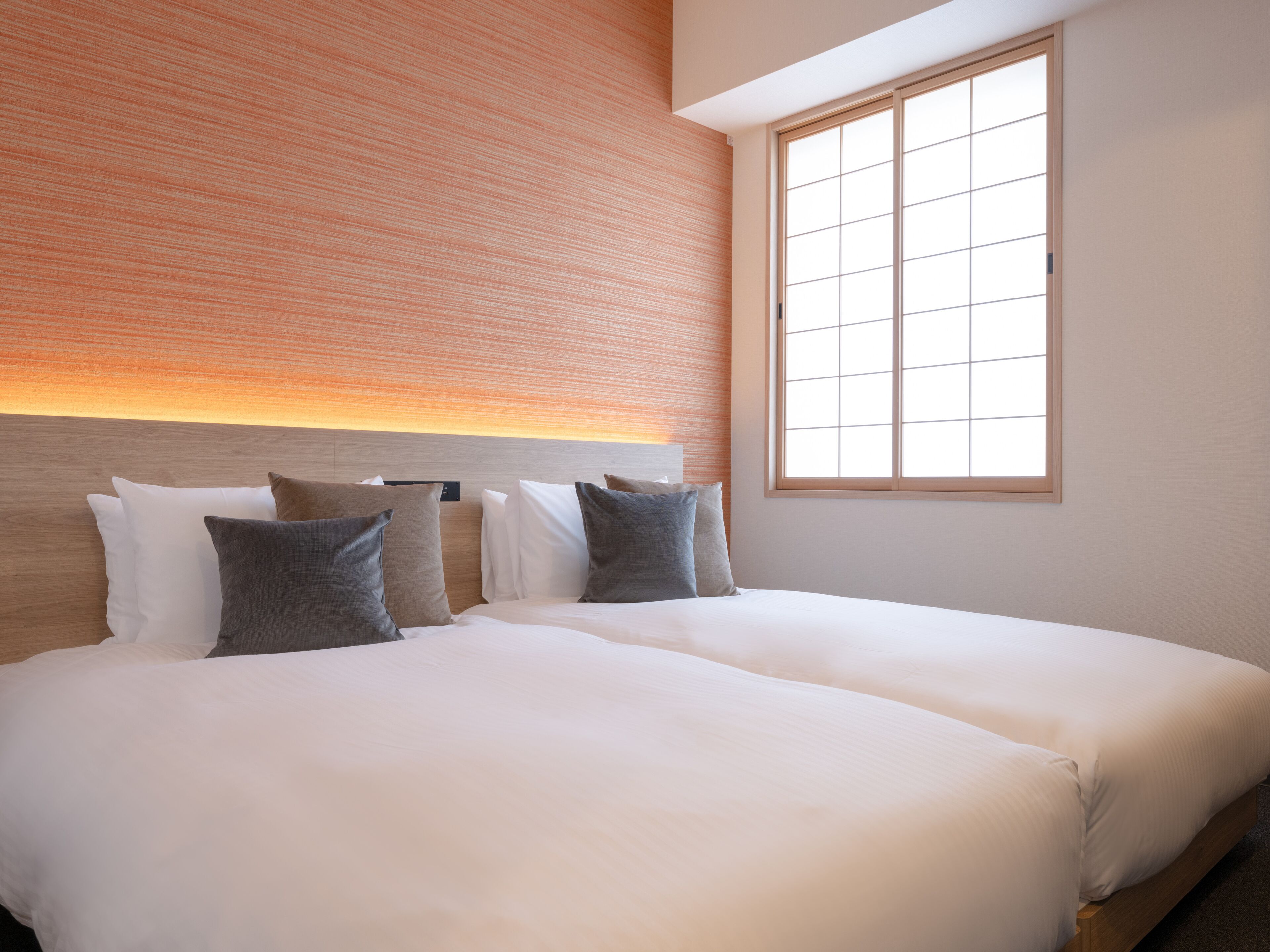 A hotel room with two beds, a brick wall, and a large window.