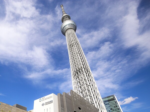 Una torre alta con una aguja distintiva y una fachada de entramado, rodeada de edificios modernos y un cielo azul despejado.