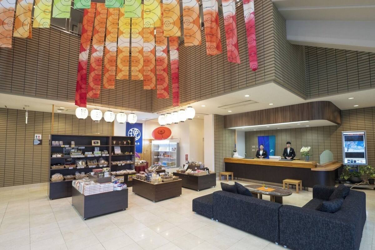 A modern hotel lobby with a reception desk, seating area, and display shelves.
