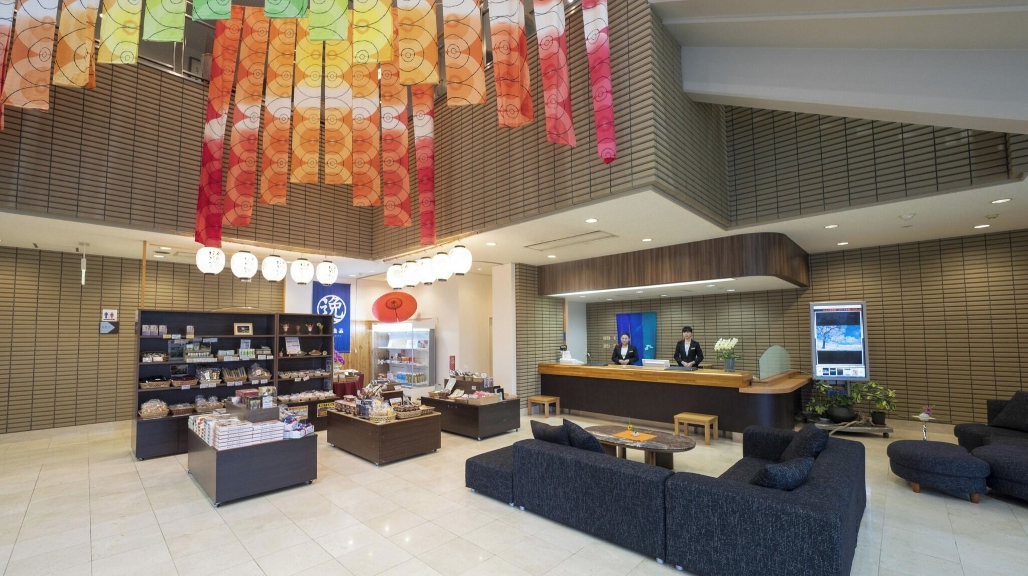 A modern hotel lobby with a reception desk, seating area, and display shelves.
