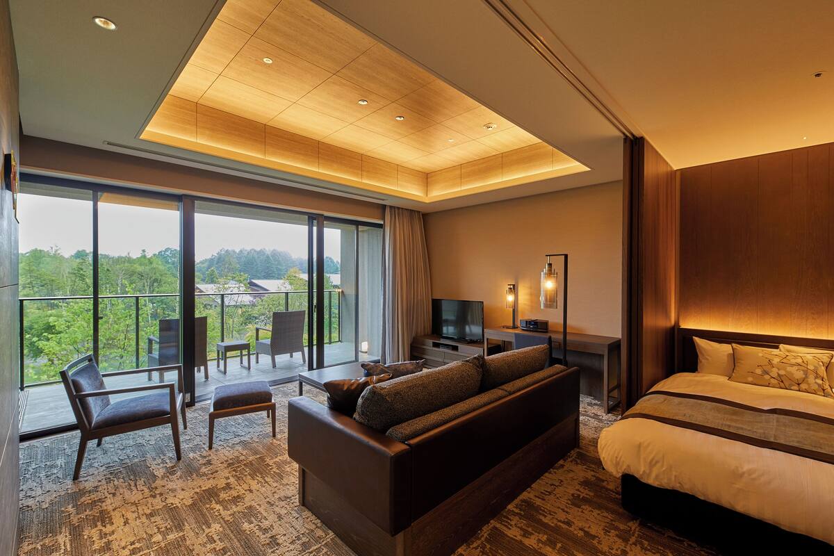 Quarto de hotel moderno com uma cama grande, um sofá, uma televisão e uma varanda com vista.