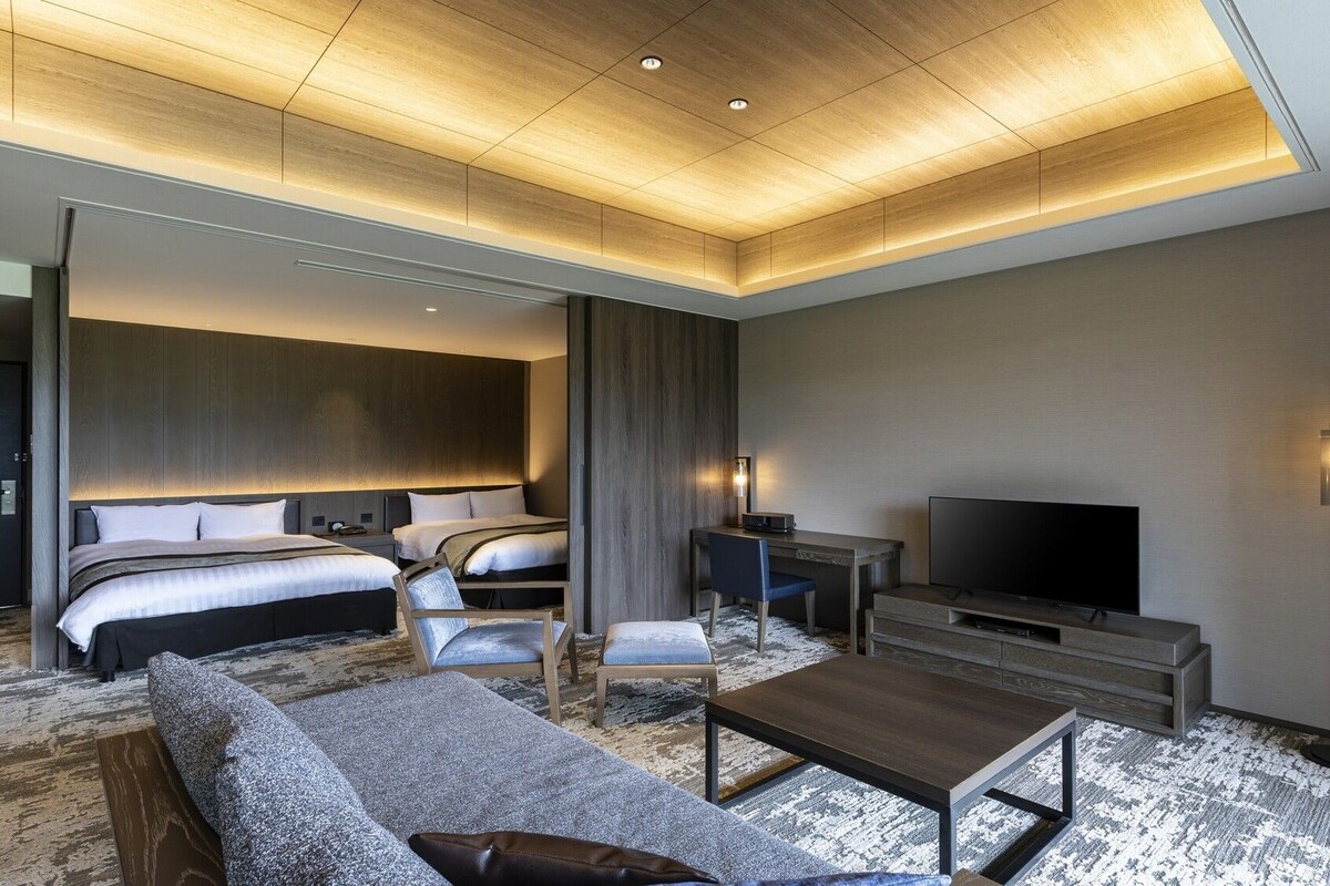 A modern hotel room with a large bed, a sofa, a TV, and a desk.