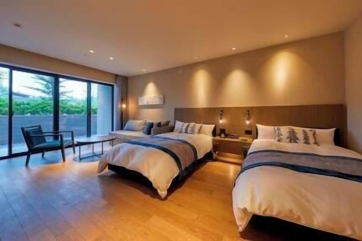 Quarto de hotel moderno com duas camas, um espaço para sentar e janelas grandes.
