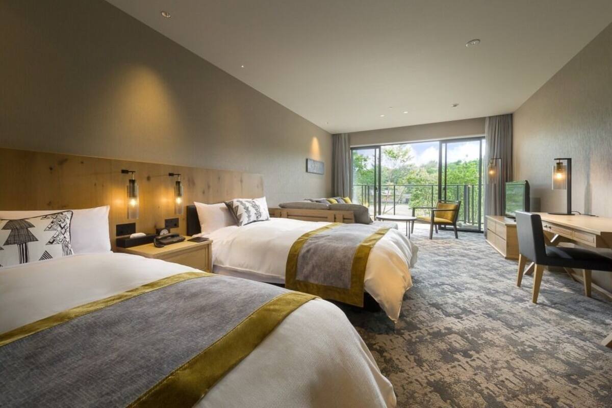 Quarto de hotel com duas camas, uma escrivaninha e varanda com vista.
