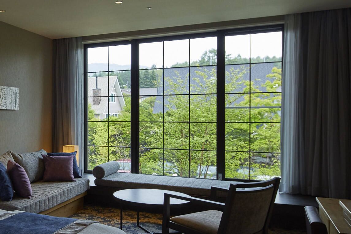 A room with a large window, a sofa, a small table, and a chair.
