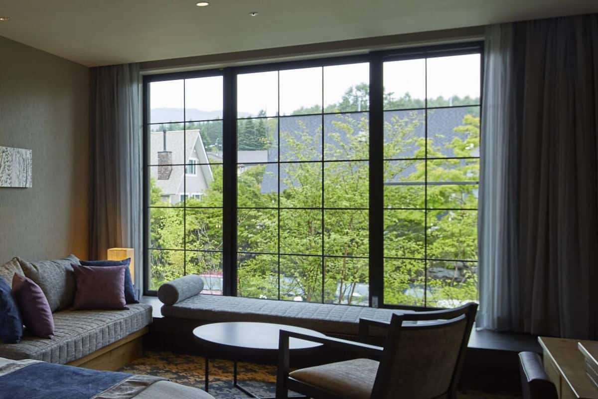 A room with a large window, a sofa, a small table, and a chair.