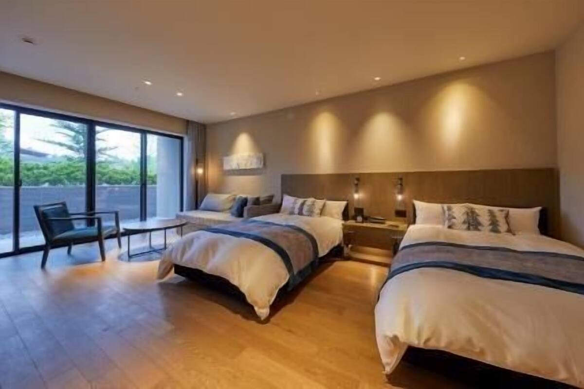 Quarto de hotel moderno com duas camas, uma pequena mesa e uma cadeira.