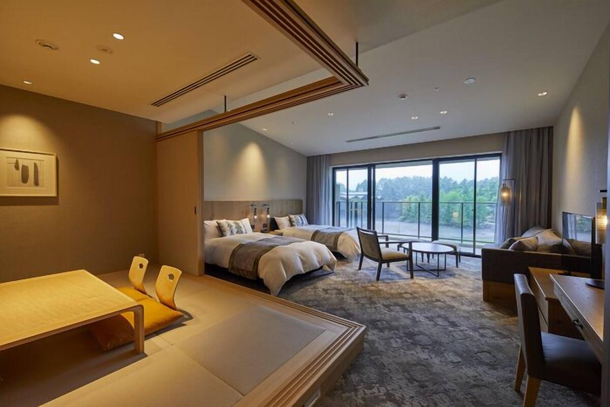 Quarto de hotel moderno com uma cama grande, uma escrivaninha, uma cadeira e vista para o exterior.
