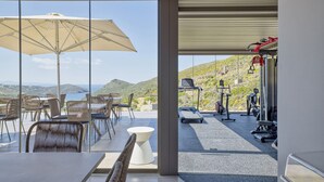 A modern outdoor dining area with a large umbrella, overlooking a scenic landscape with hills and a body of water. - Infinite Serenity: Villa Etheria – 4 Bed Luxury, Private pool, Gym (Andros)