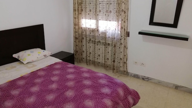 A bedroom with a bed, a nightstand, a mirror, and a window with curtains. - Holiday rentals in Tunis (Tunis)