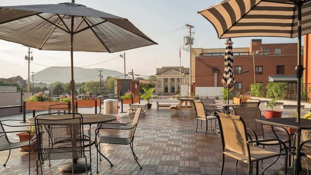 An outdoor patio with tables and chairs, surrounded by potted plants and umbrellas. - Stay Roanoke | Luxe rooftop retreat in downtown (Roanoke)