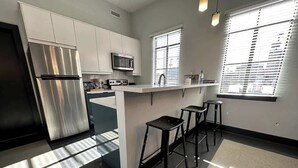 A modern kitchen with a stainless steel refrigerator, a microwave, a sink, and a bar area with stools. - Stay Roanoke | Luxe rooftop retreat in downtown (Roanoke)