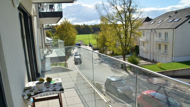 A balcony with a table, chairs, and potted plants. - New 50m² apartment in Bertrange with basement parking (Bertrange)