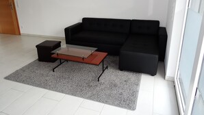 A modern living room with a black sofa, a glass-top coffee table, and a grey rug. - New 50m² apartment in Bertrange with basement parking (Bertrange)