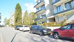 A street with parked cars and modern apartment buildings. - New 50m² apartment in Bertrange with basement parking (Bertrange)