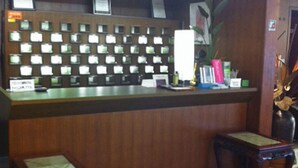 A reception desk with a wooden panel and a series of small windows. - Kawanoe Business Hotel (Shikokuchuo)