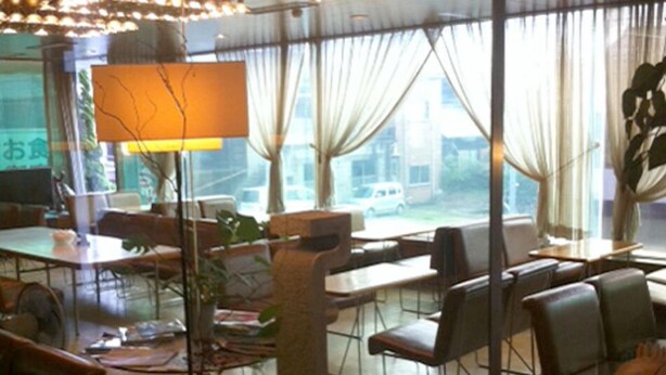 A restaurant with a large window, tables, chairs, and a lamp. - Kawanoe Business Hotel (Shikokuchuo)