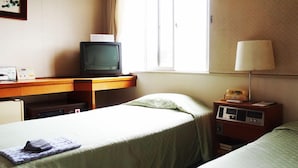 A hotel room with a bed, a desk with a television, a lamp, and a bedside table with a telephone. - Kawanoe Business Hotel (Shikokuchuo)