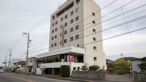 A multi-story hotel with a modern facade, a visible entrance, and a parking lot in the foreground. - Kawanoe Business Hotel (Shikokuchuo)