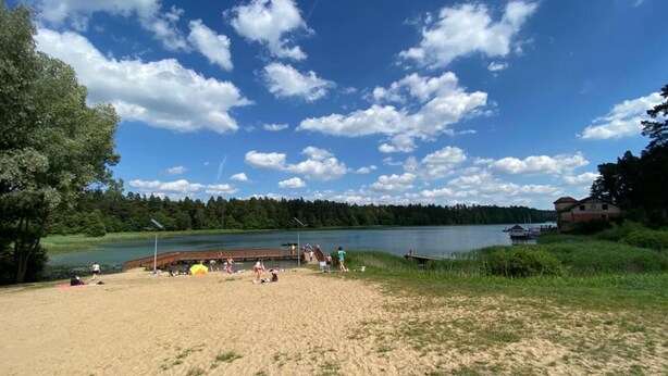 A beach with a wooden pier extending into a lake, surrounded by trees and a clear sky. - Delightful SPA Cottage With Fire Place and Sauna (Grunwald)
