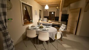 A dining area with a round table set for four, white chairs, a clock on the wall, and a wooden ceiling. - Delightful SPA Cottage With Fire Place and Sauna (Grunwald)