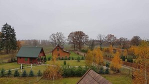 A rural setting with two wooden cabins surrounded by trees and a grassy field. - Delightful SPA Cottage With Fire Place and Sauna (Grunwald)