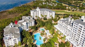 Een resort met meerdere hoge gebouwen, een zwembad in het midden en een golfbaan op de achtergrond.