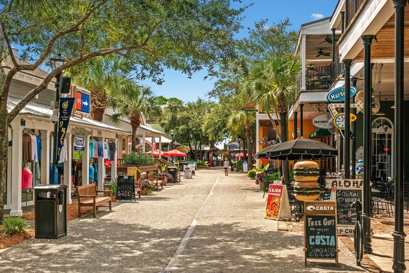Calle bordeada de tiendas y terrazas, con palmeras y cielo despejado.