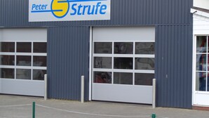 A building with a sign reading "Peter Strufe" and a large garage door. - First floor vacation apartment Roseneck on the North Sea in Schleswig-Holstein, (Friedrichskoog)