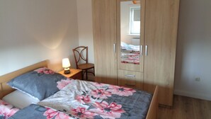 A bedroom with a wooden wardrobe, a bed with floral bedding, a chair, and a table lamp. - First floor vacation apartment Roseneck on the North Sea in Schleswig-Holstein, (Friedrichskoog)
