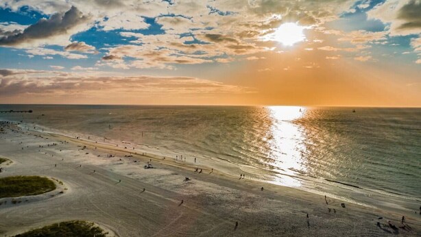 Una playa con cielo despejado y el sol poniéndose en el horizonte.
