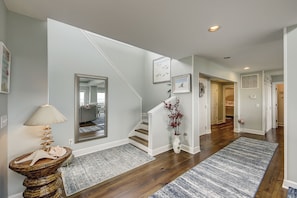 A hallway with a staircase, wooden flooring, and a decorative vase with red flowers. - 33 Sandpiper- Oceanfront, The NEW Daisy.  LARGE Private Pool & Fire Pit (Hilton Head Island)