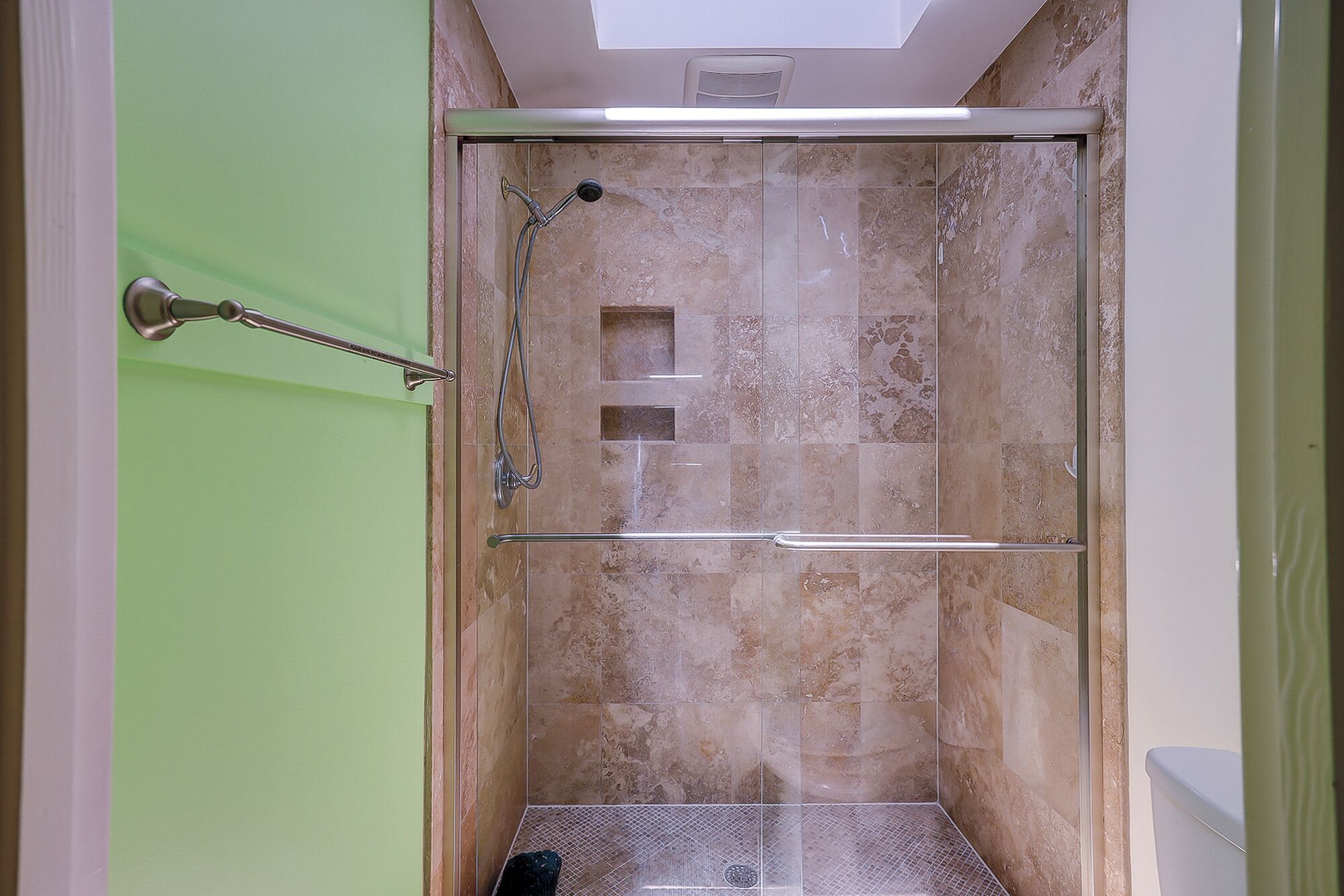 A shower with a glass door, a towel rack, and a small square vent on the wall.