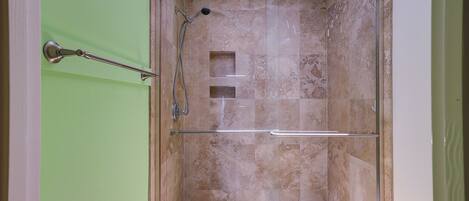 A shower with a glass door, a towel rack, and a small square vent on the wall.