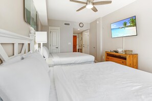 Une chambre avec deux lits, un ventilateur de plafond, un téléviseur fixé au mur et une commode en bois.