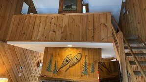 Ein Holzinnenraum mit einer erhöhten Galerie, einem Kamin mit Verzierungen und einer Treppe.