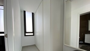 Un pasillo estrecho con paredes blancas, una ventana pequeña y una puerta a la izquierda.