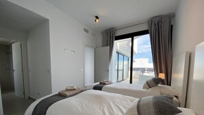 Una habitación de hotel moderna con dos camas, un ventanal con cortinas, vistas a la ciudad y un balcón.