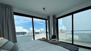 Habitación de hotel moderna con una cama grande, una silla y vistas de la ciudad a través de amplias ventanas.