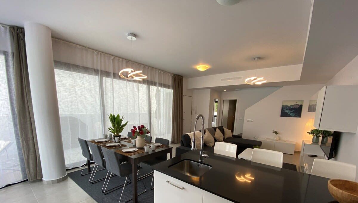A modern kitchen with a central island, dining area with chairs, and a view of the outdoors through large windows.