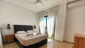 Ein Schlafzimmer mit einem Bett, Nachttischen, einem Deckenventilator und Blick ins Freie.