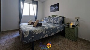 Une chambre à coucher avec un lit, une table de chevet, une lampe fixée au mur et une fenêtre avec des rideaux.