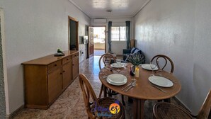 Un coin repas avec une table ronde dressée pour quatre personnes, un buffet en bois et une vue sur le salon par une porte ouverte.
