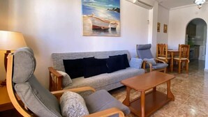 A living room with a sofa, two armchairs, a coffee table, and a painting of a beach scene. - 2-Bed Ground-Floor Apt in La Cinuelica R2 L188 (Orihuela)