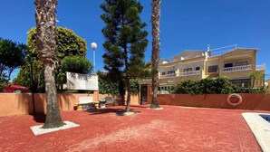 A hotel with a red-tiled courtyard, palm trees, and a two-story building with balconies. - 2-Bed Ground-Floor Apt in La Cinuelica R2 L188 (Orihuela)