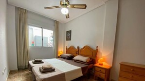 A hotel room with a large bed, two bedside tables, a wooden dresser, and a ceiling fan. - 2-Bed Ground-Floor Apt in La Cinuelica R2 L188 (Orihuela)